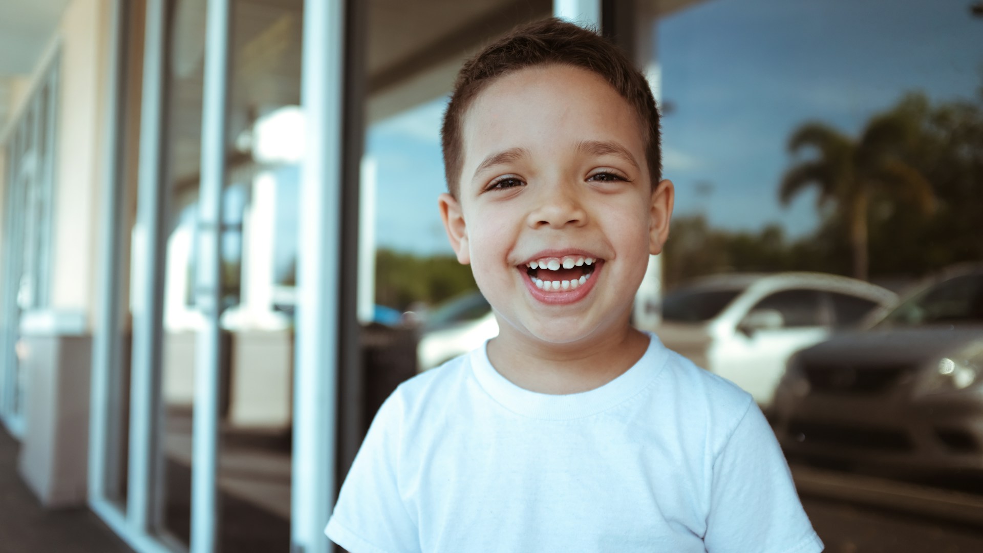 Smiling young boy standing outdoors in a white t-shirt, symbolising joyful and inclusive experiences at neurodivergent-friendly attractions in London