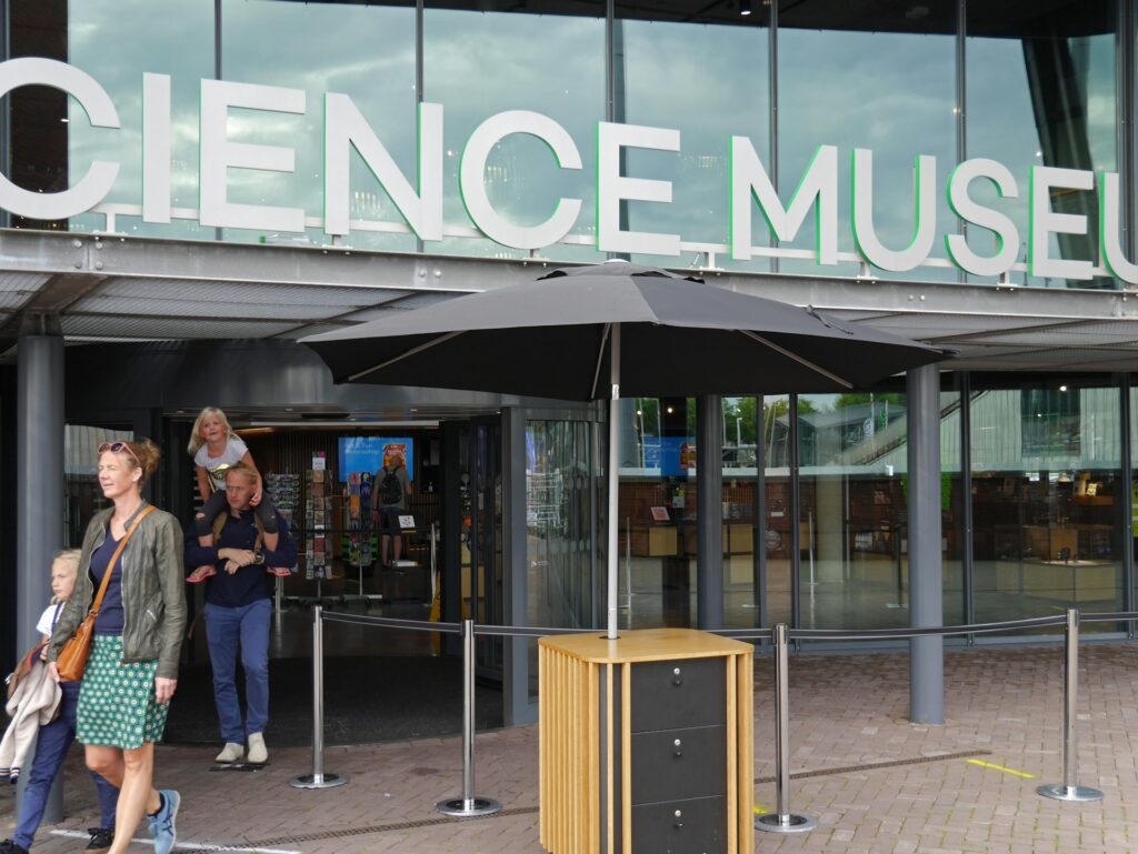 Visitors entering the main entrance of the Science Museum in London, with large black signs on either side of the doorway