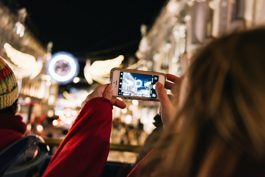 Person taking a photo of London Christmas lights from the top deck of an open-top bus during a festive tour.